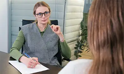 A woman engaged in individual therapy, writing notes at a desk with a pen and paper during her drug rehabilitation process