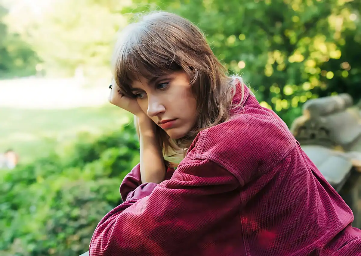 A woman in a red jacket sits on a bench struggling from bipolar disorder