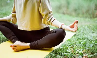 A woman meditates in a yoga position on a grassy field, symbolizing mindfulness in addiction treatment and recovery