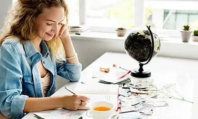 A woman seated at a desk, engaged with her notebook and coffee, contemplating her path to self-discovery