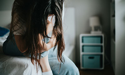 A woman seated on a bed in a serene bedroom, reflecting on her journey through anxiety treatment in Los Angeles.