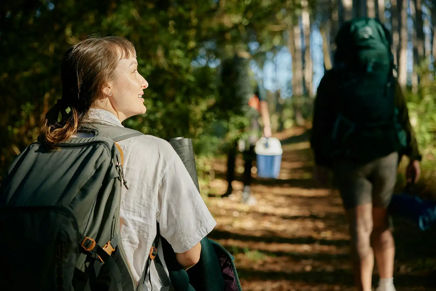 A woman traverses a forest trail with a backpack, enjoying the peaceful atmosphere and vibrant foliage around her