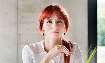 A woman with vibrant red hair sits at a table, engaged in deep thought about her path to self-discovery and realization.