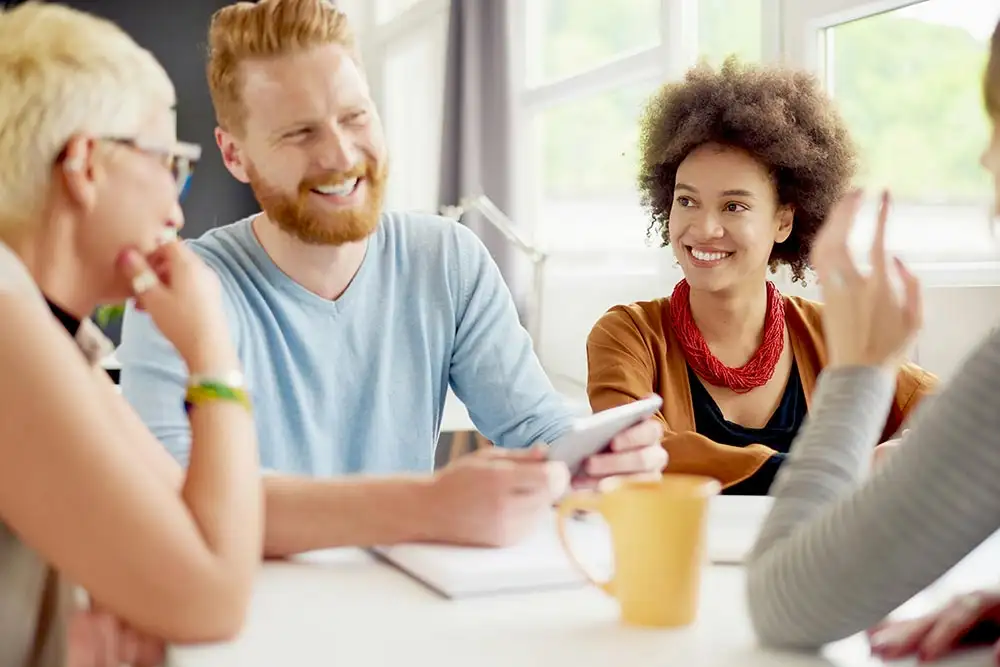 four people at a table, one smiling, showcasing a moment of joy and connection in a sober living community