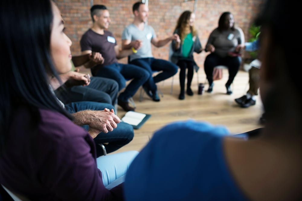 men and women sitting in a room, holding hands during a spiritual 12 step program at Riverside Inpatient Rehab