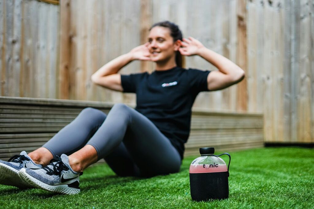 A woman rests on the grass with her hands on her head taking a break after completing her sit up routine