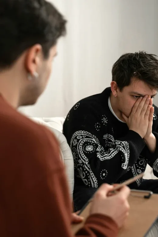 A man sits on a couch, hands on his face, reflecting on resentments during his drug rehabilitation journey