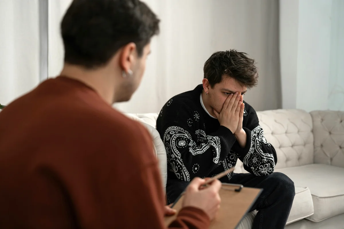 A man sits on a couch, hands on his face, reflecting on resentments during his drug rehabilitation journey