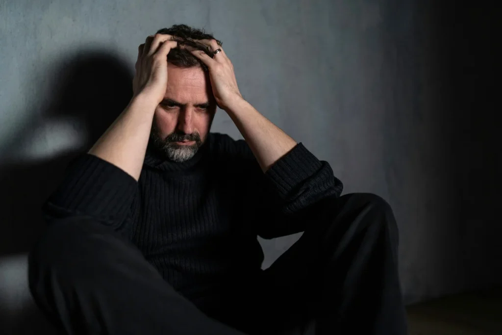 man wearing black sweater and pants sitting in a dark room in riverside California having resentments in addiction recovery