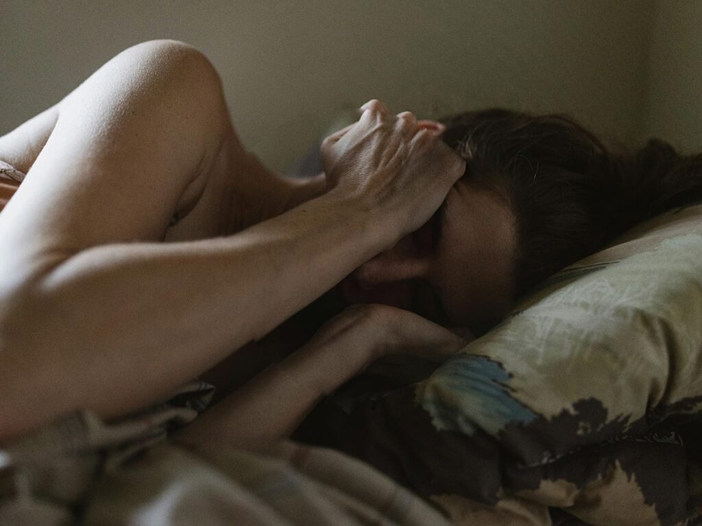 a woman suffering from anxiety lying on bed with her hands on her head