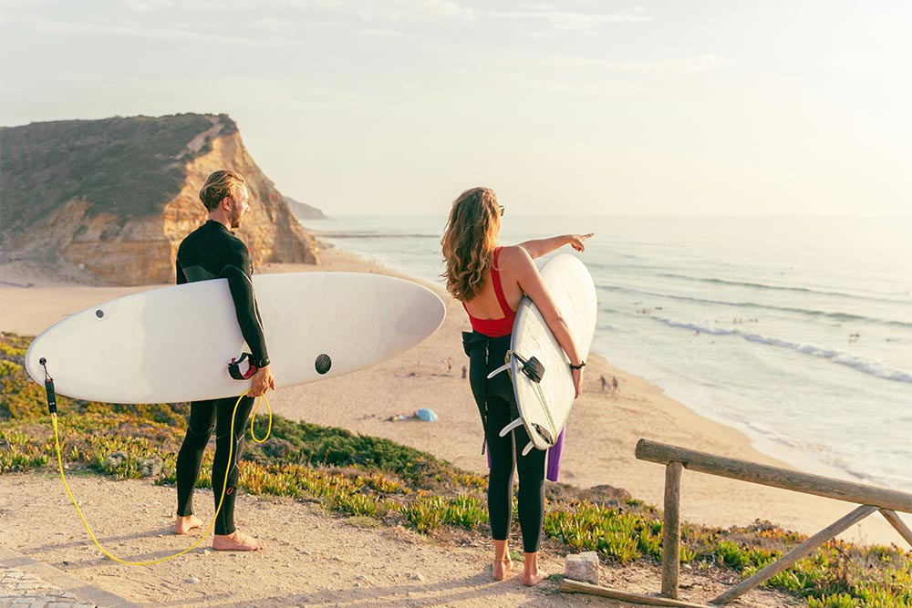 a man and a woman carrying their surf board in Souther California beach