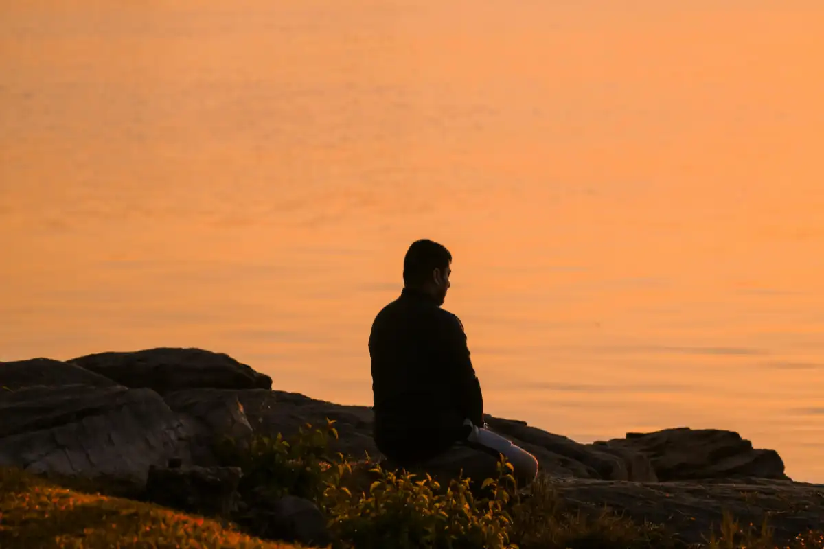 man sitting on a rocky hill meditating near the ocean