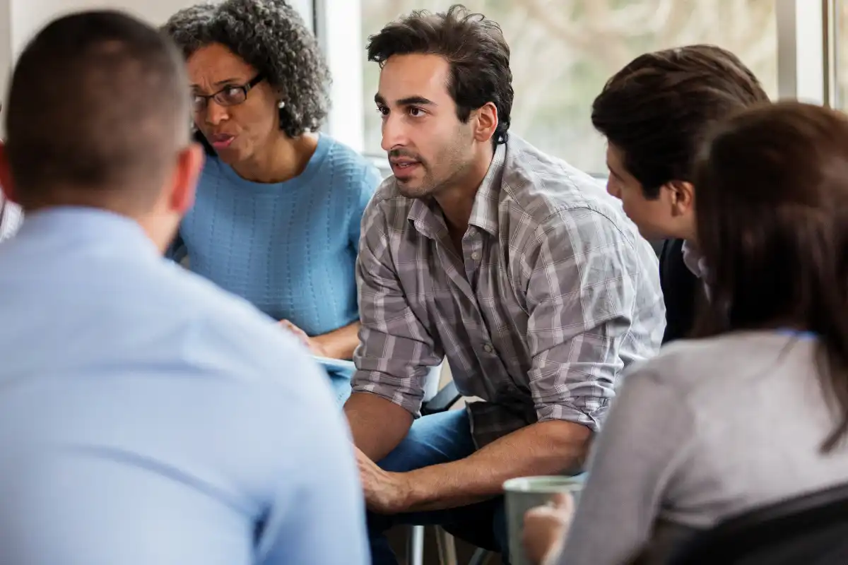 Vulnerable mid adult man talks in group therapy meeting