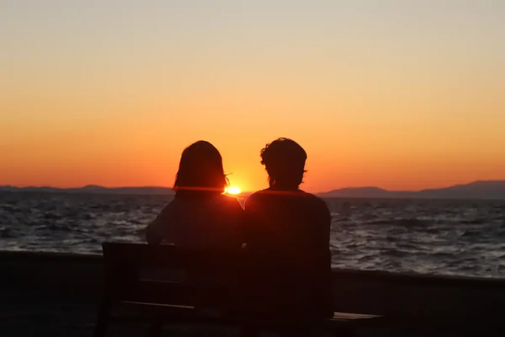 Silhouette of a Couple Sitting on Bench in Front of the Sea during Sunset