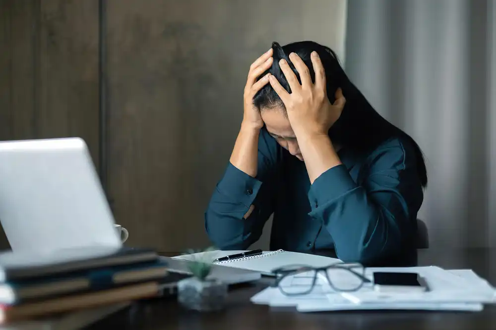 Frustrated woman with head in hands sitting at desk