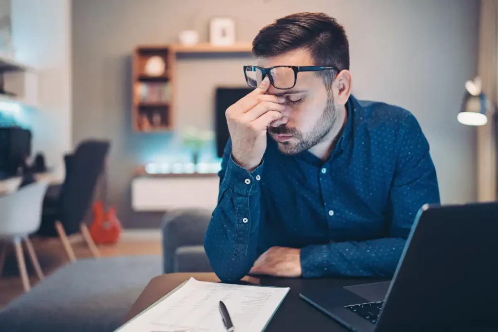 Businessman with a headache, using laptop and doing paperwork at home