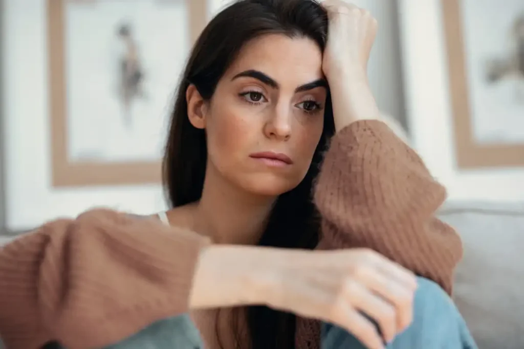 Depressed young woman overthinking while sitting on the couch at home