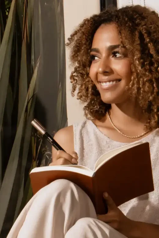 Woman sitting on window seat indoors journaling about addiction recovery